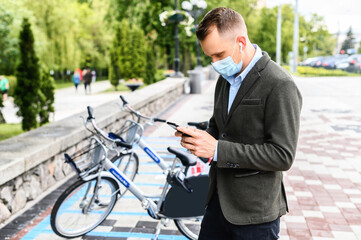 A young guy with medical mask in smart casual wear going to rent city bike. The guy gets to work without using public transport