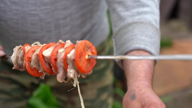 Mature man impales raw shashlik on skewer. Close up of men's hands hold skewer with barbecue. Concept of picnic outdoor.
