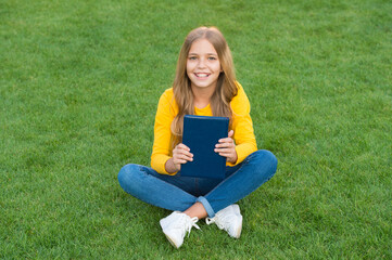 Fototapeta premium teen girl inspired with new book. relax on green grass. spring leisure time. happy childhood. kid read book outdoor in park. happy little girl study on holiday. kid beauty and fashion