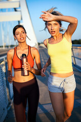 Beautiful women in sportswear drinking water, talking and resting after training outdoors