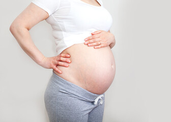 Pregnant girl with a bare belly in a white T-shirt and gray pants on a light background