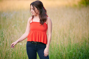Beautiful young woman in red blouse standing in field of tall grass