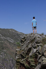 A boy standing on a spur of rock observes a panorama of morenic hills