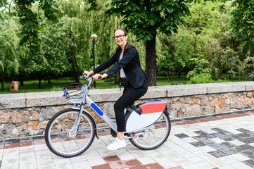 Contemporary businesswoman is riding for work on a bicycle. Young woman in smart casual wear riding bike in the city