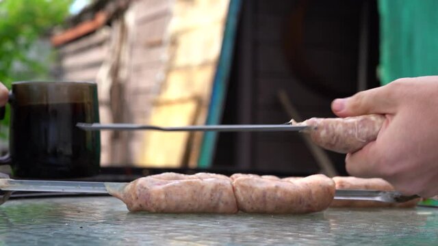 Man impales raw sausages on skewer. Close up of men's hands hold skewer with frankfurters. Concept of picnic outdoor.