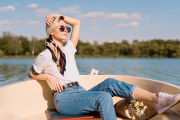 Pretty amazing young woman, blond relaxing on a boat, wearing sunglasses, enjoying her vacation and amazing time