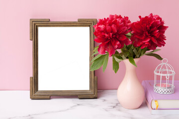 Fragment of an interior with an empty mock up photo frame, a vase with peonies and books
