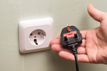 Different standards for electrical outlets. Unsuitable connector and plug in the hand of a person....