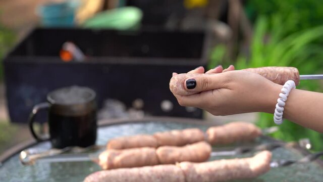 Woman impales raw sausages on skewer. Close up of woman's hands hold skewer with frankfurters. Concept of picnic outdoor