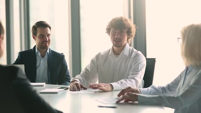 In modern boardroom gathered diverse business partners businesspeople listening man team leader offers share ideas during morning briefing or negotiations. Leadership, teamwork and cooperation concept