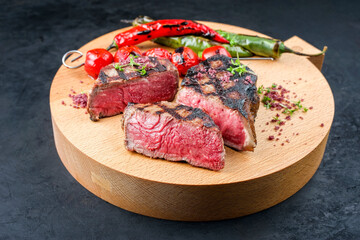 Barbecue dry aged wagyu roast beef steak with tomatoes and chili as closeup on a modern design wooden board