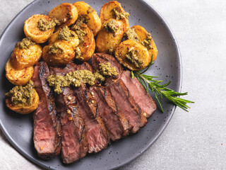 Sliced juicy grilled steak medium rare beef on the plate with roasted potatoes sauce pesto