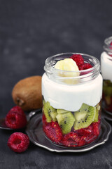 Healthy snack with raw raspberry and kiwi fruits and yoghurt layered in glass on dark background