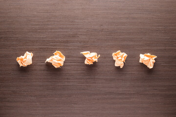 Five crumpled pieces of paper in a row on a wooden table.
