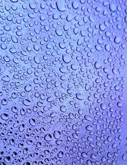 After the rains, raindrops on the glass formed a natural textural pattern. Rainwater gathered in drops on the clear glass of the window. Textured background. Purple toning