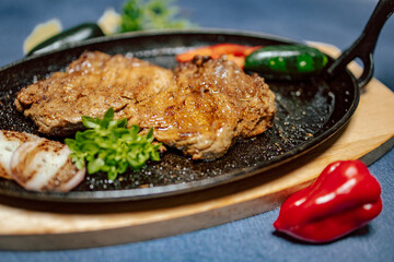 Piece of grilled steak with paprika and onion as side dish on black pan