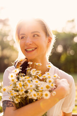 Portrait of a Sunny woman embracing a bunch of chamomile with the sun rays on her face enjoying life