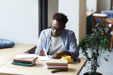 Obraz premium Hardworking African American student working on research in university canteen