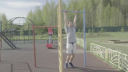 Man works out outdoor. Young adult male does training exercises on the bar. He pulls up, pushes up with clap, and does a hanging leg raise. Flat log profile, without color grading