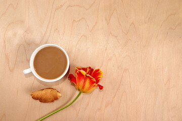 A cup of hot latte coffee and flowers on a sunny wooden table, selective focus, flat lay, copy space. Work desk of a modern woman, home office, space for text. Minimal holiday concept.