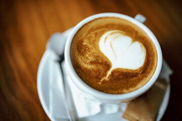 Close-up of fresh cappuccino on the table in white cup heart foam shape.