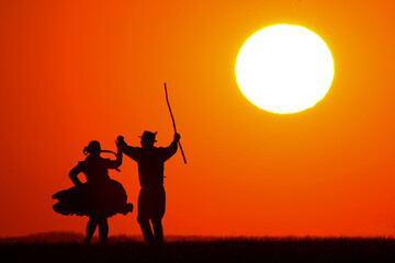 A man and woman in traditional folk costume dancing at a wonderful sunset showing his silhouette