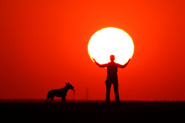 woman holding the sun with her hands, her dog looking at her.