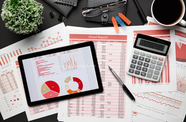 Top view of modern black office desk with tablet pc and financial reports, notebook, pencil and a lot of things. Flat lay table layout.