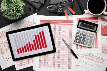 Top view of modern black office desk with tablet pc and financial reports, notebook, pencil and a...