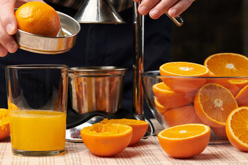 Squeezing an orange with a manual press, close view, making a glass of fresh. Fresh oranges on a wooden table, whole, squeezed and sliced.