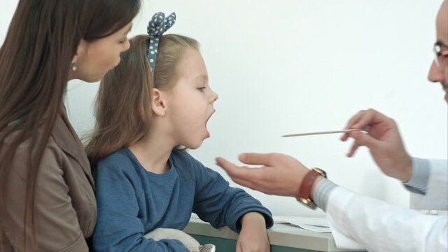 Little girl having throat examination with tongue depressor by a male doctor