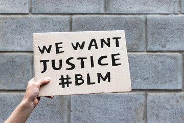 Hand holding cardboard banner with text We Want Justice, hashtag BLM, Black Lives Matter. Anti-racism protest.