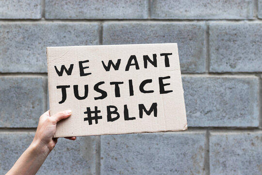 Hand holding cardboard banner with text We Want Justice, hashtag BLM, Black Lives Matter. Anti-racism protest.