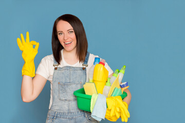 Beautiful woman cleaning lady with a bucket full of colorful detergent in rubber gloves, looking at the camera.
Copy space, isolated blue background.