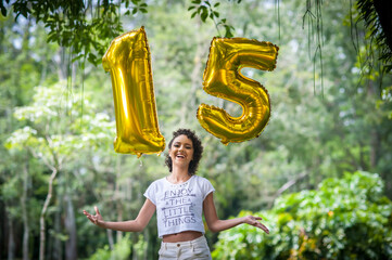brazilian teenager girl in the park trowing up  balloons number 15  in celebration of her fifteenth...