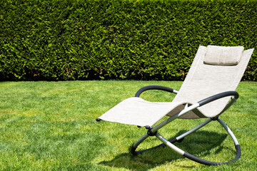 Biege rocking lounger on a green grass. Lounger outdoor, space for text