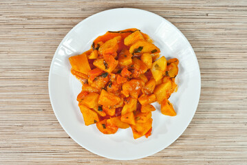 Potatoes in a white plate on a wooden table. Boiled potatoes with orange sauce. Place for text near the plate. Copy space for design.