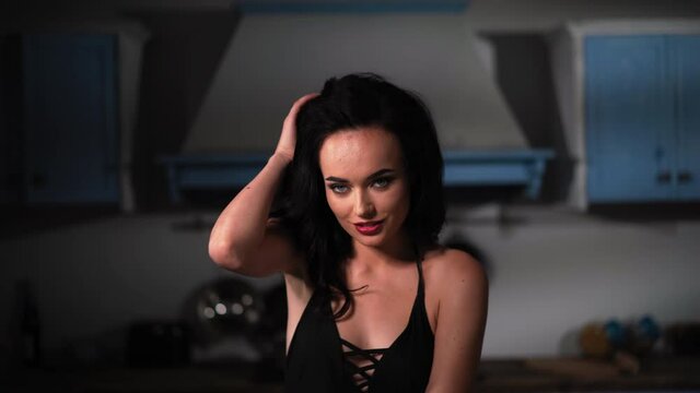 Passionate girl wearing black bodysuit touching sensually her hair moving it side of her beautiful face sitting on kitchen island table. Shoulder close up. Prores 422.