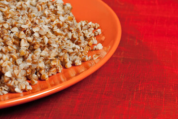 Buckwheat orange plate on a wooden table. Food in utensils on a background of old red plywood. Place for text near the plate. Copy space for design.