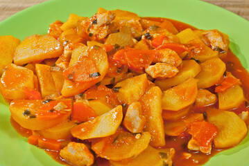 Potatoes in a green plate on a wooden table. Boiled potatoes with orange sauce.