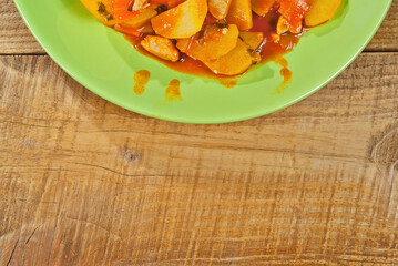 Potatoes in a green plate on a wooden table. Boiled potatoes with orange sauce. Place for text near the plate. Copy space for design.