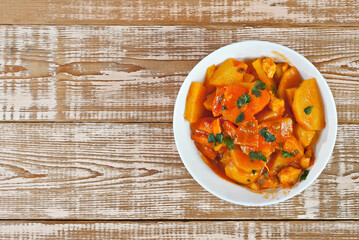 Potatoes in a white bowl on a wooden table. Boiled potatoes with orange sauce on a pink shabby board. Place for text near the plate. Copy space for design.