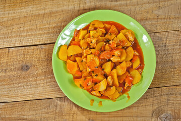 Potatoes in a green plate on a wooden table. Boiled potatoes with orange sauce. Place for text near the plate. Copy space for design.