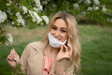 Young blond woman in mask holding an apple tree flower. High quality photo