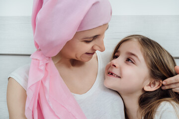 Cancer mother with a pink headscarf looks tenderly at her blonde daughter