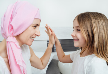 Cancer mother with a pink headscarf high-fives her blonde daughter