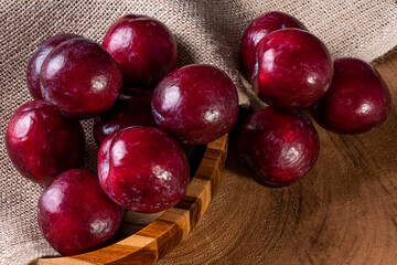 Some plums in a basket with jute fabric. Wood background