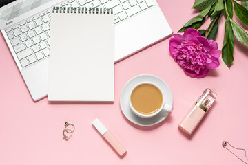Obraz na płótnie Canvas Woman’s home office desktop with laptop, blank notepad, cup of coffee, perfumes and beautiful peony flower. Work from home concept.
