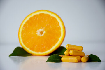 Fototapeta premium VItamin C capsules with orange on background. Natural supplements, antioxidants, prevention, immunity, treatment concept.