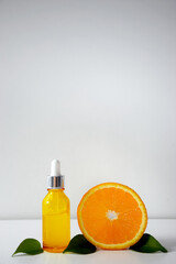 Vitamin C peeling or serum in bottle and orange citrus with green leaves on white background. Face care, anti-aging, exfoliating cosmetic. Citrus essential oil, aromatherapy. Copy space.